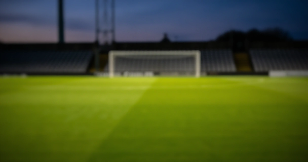 Tyhjä Valioliiga-stadion hämärässä, nurmikentän vihreä väri korostuu valoilla