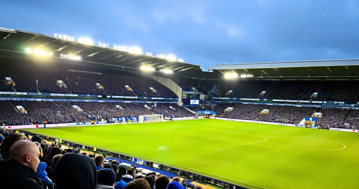 Englantilaisella jalkapallostadionilla täpötäynnä olevia katsomoja valaistuna stadionvaloilla