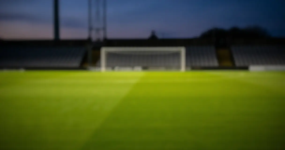 Tyhjä Valioliiga-stadion hämärässä, nurmikentän vihreä väri korostuu valoilla